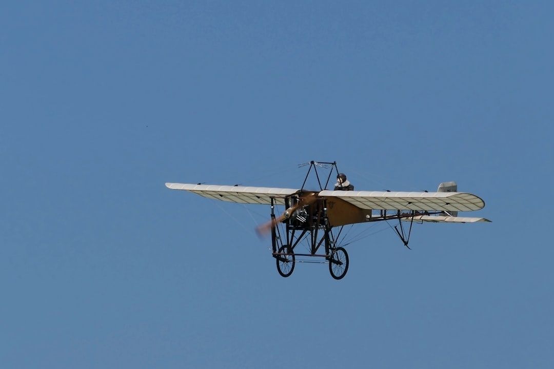 Monoplan ancien en vol, avec un pilote à bord, sur fond de ciel bleu