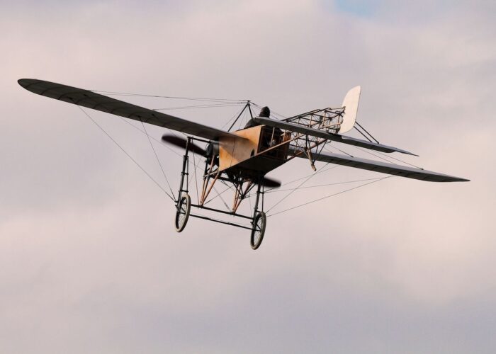 Aéroplane ancien à structure apparente volant dans un ciel pastel